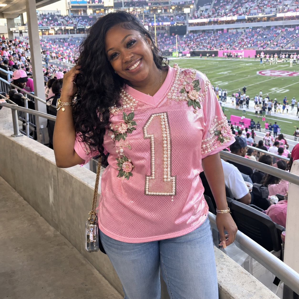 Black woman wearing a pink pearl-and-floral number one football jersey at a football stadium